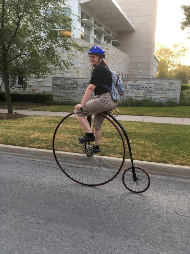 A man is riding a large bicycle on the side of the road.
