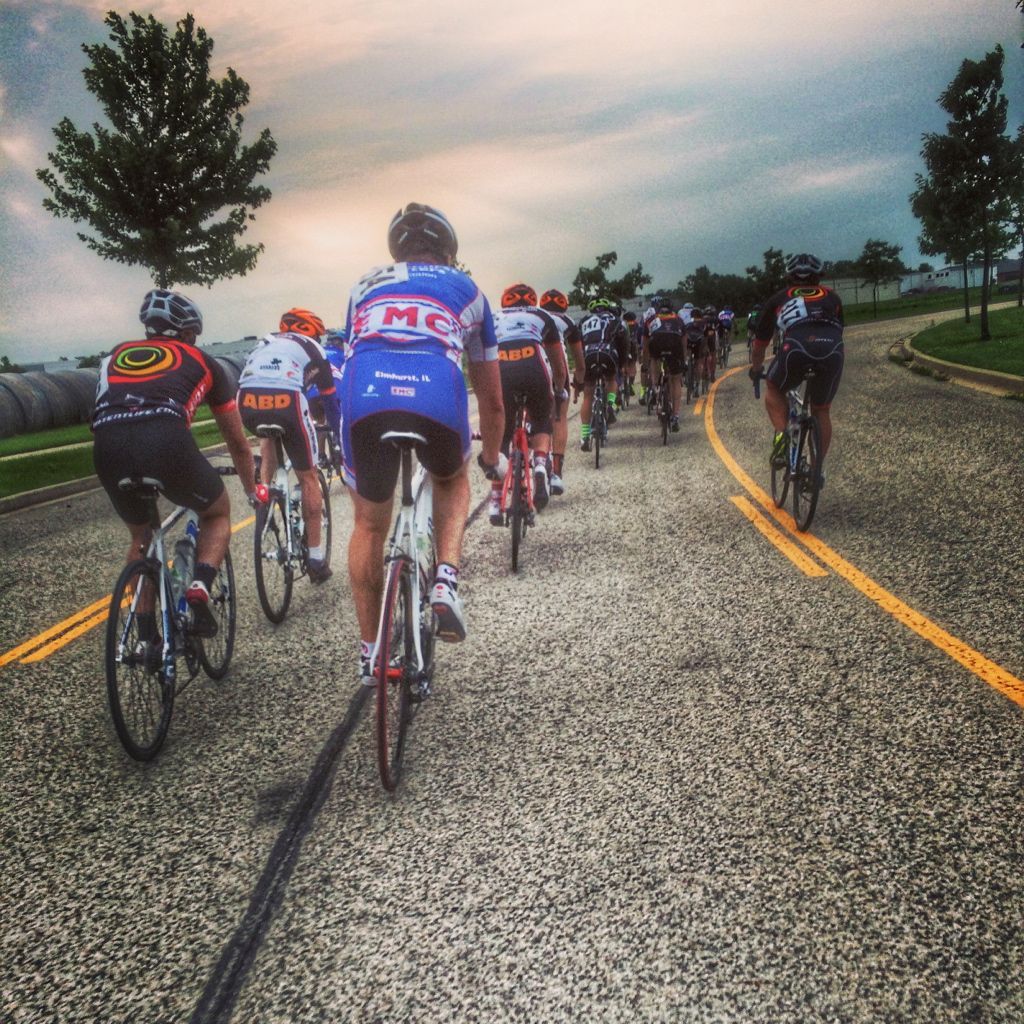 A group of cyclists are riding down a road with one wearing a shirt that says bmc