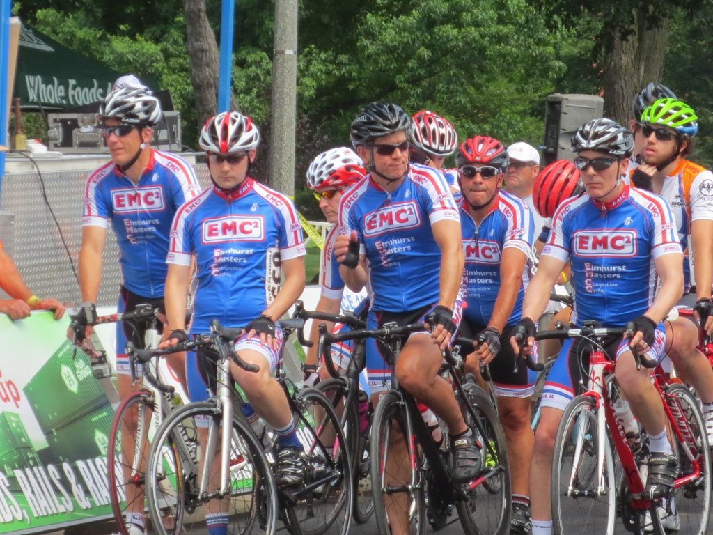 A group of cyclists wearing emc jerseys are riding down a street
