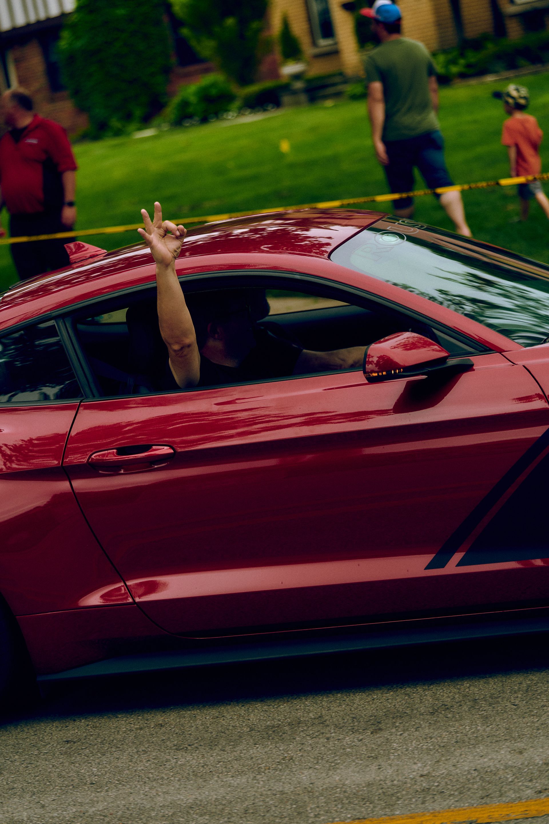 A man is waving from the window of a red car.