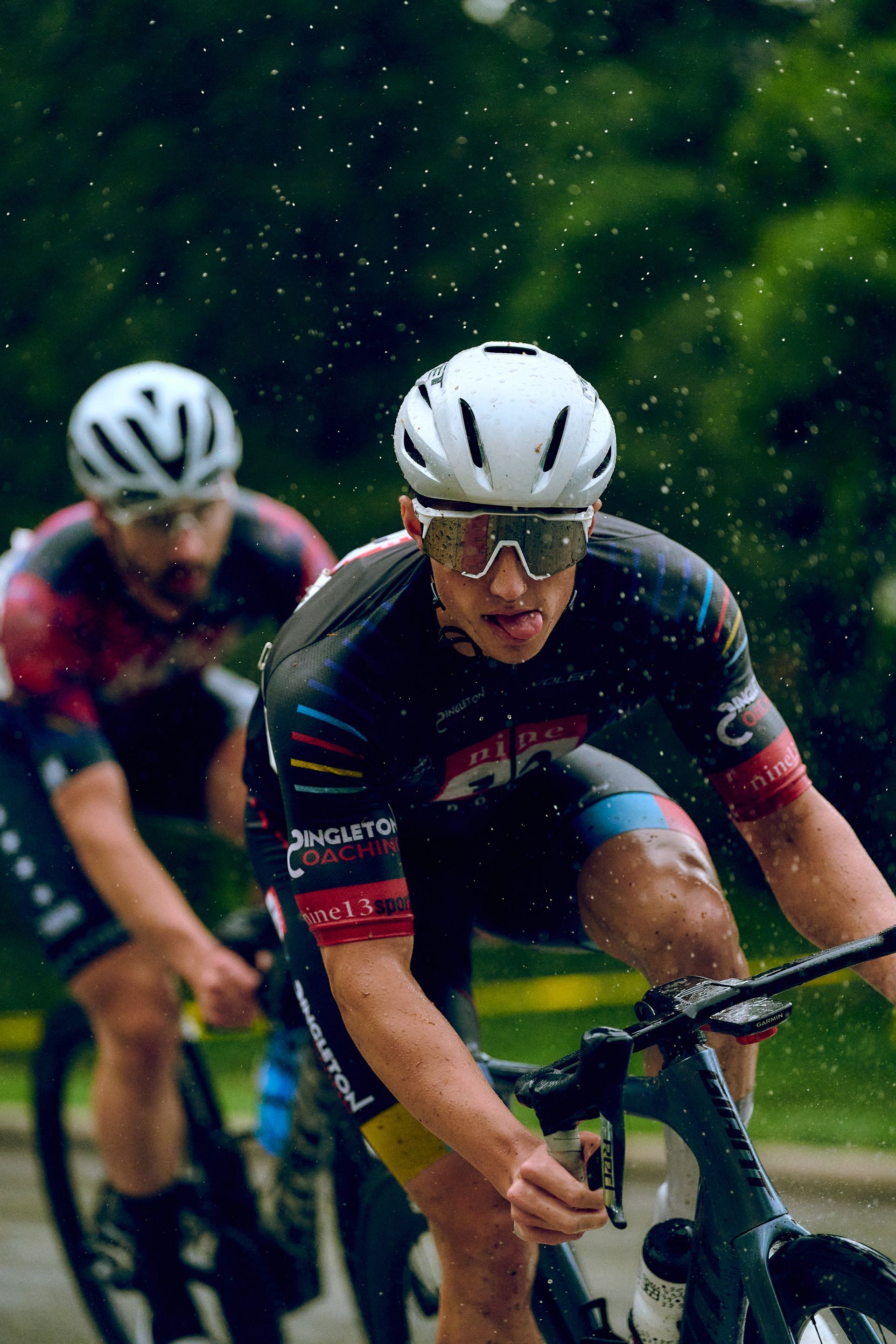 A man wearing a helmet and sunglasses is riding a bike in the rain.