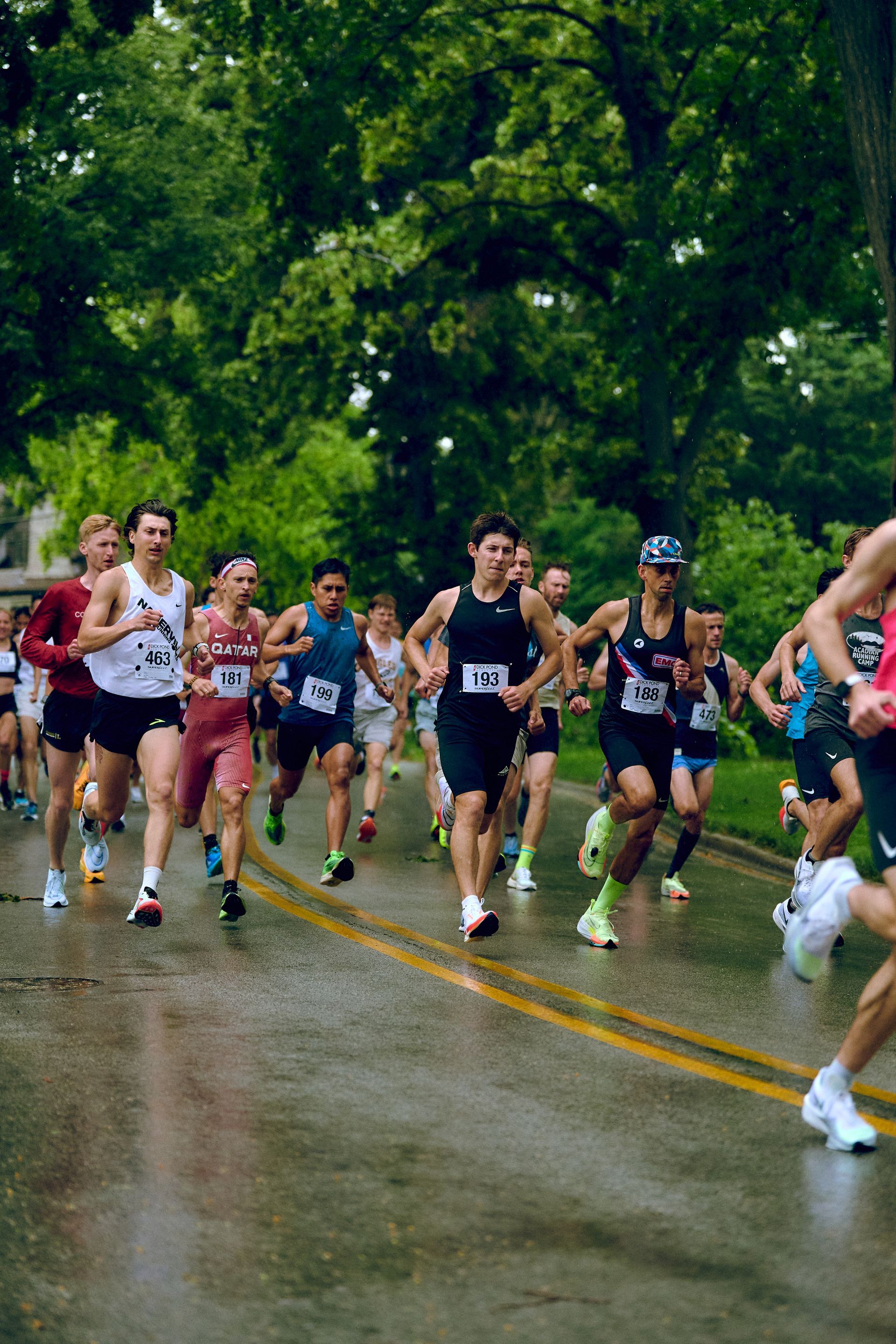 A group of people are running a marathon on a wet road.