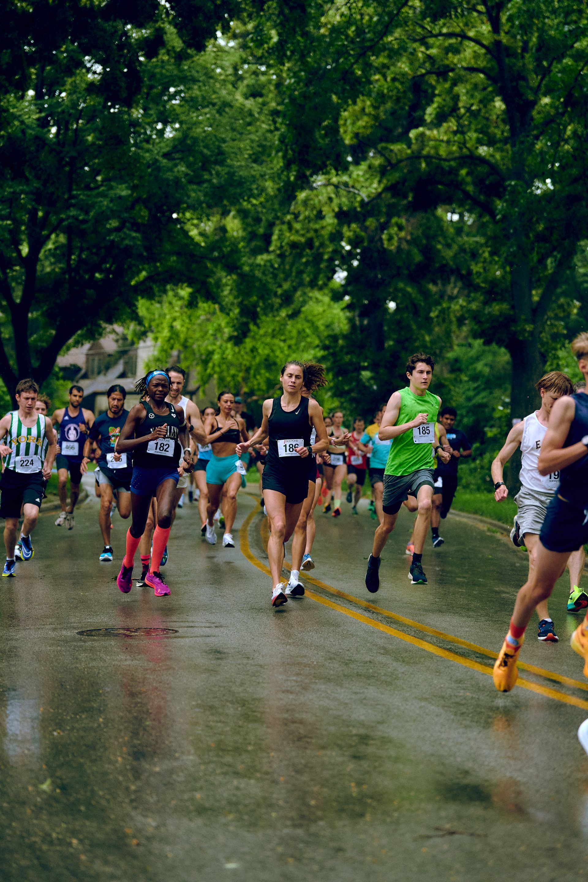A group of people are running a marathon on a wet road.