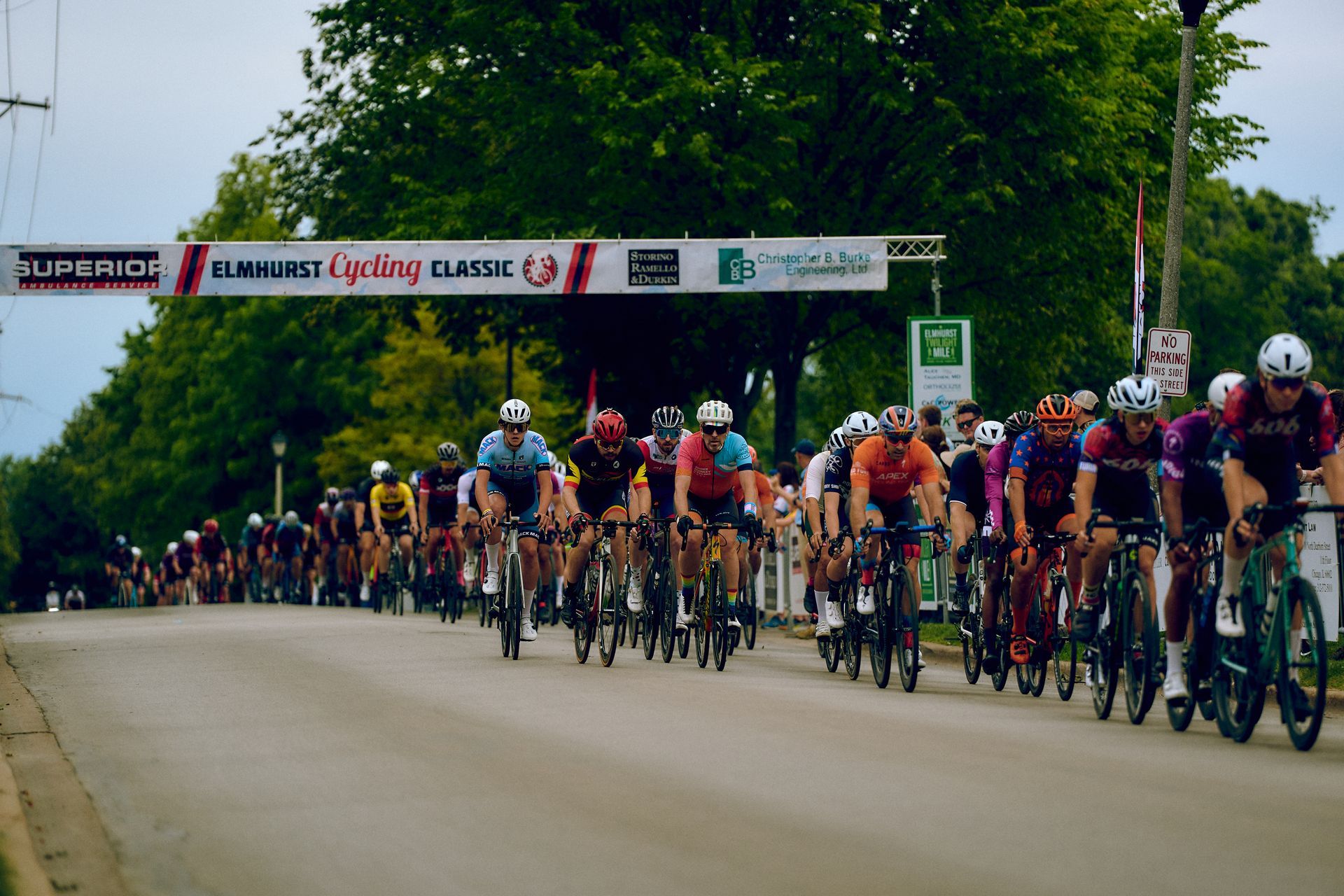 A group of cyclists are riding down a road with a sign that says elmo just cycling classic