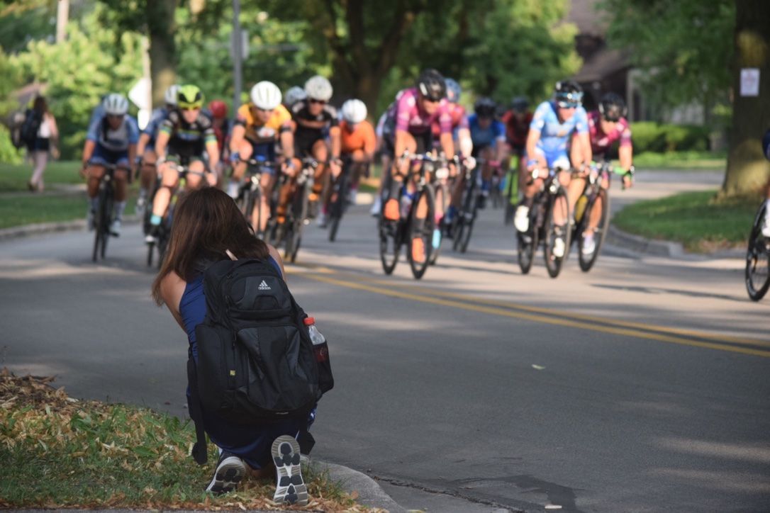 A woman is kneeling down to take a picture of a group of cyclists riding down a street.