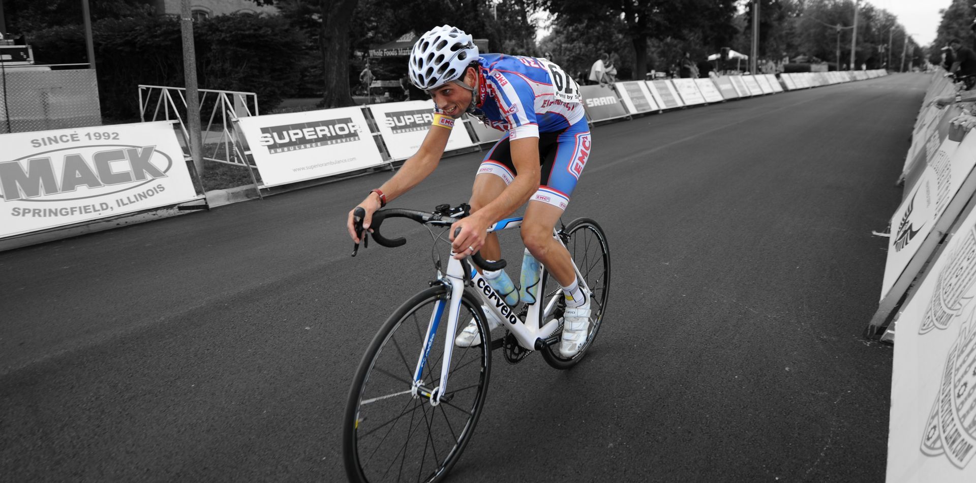 A man is riding a bike on a road with a mack sign in the background