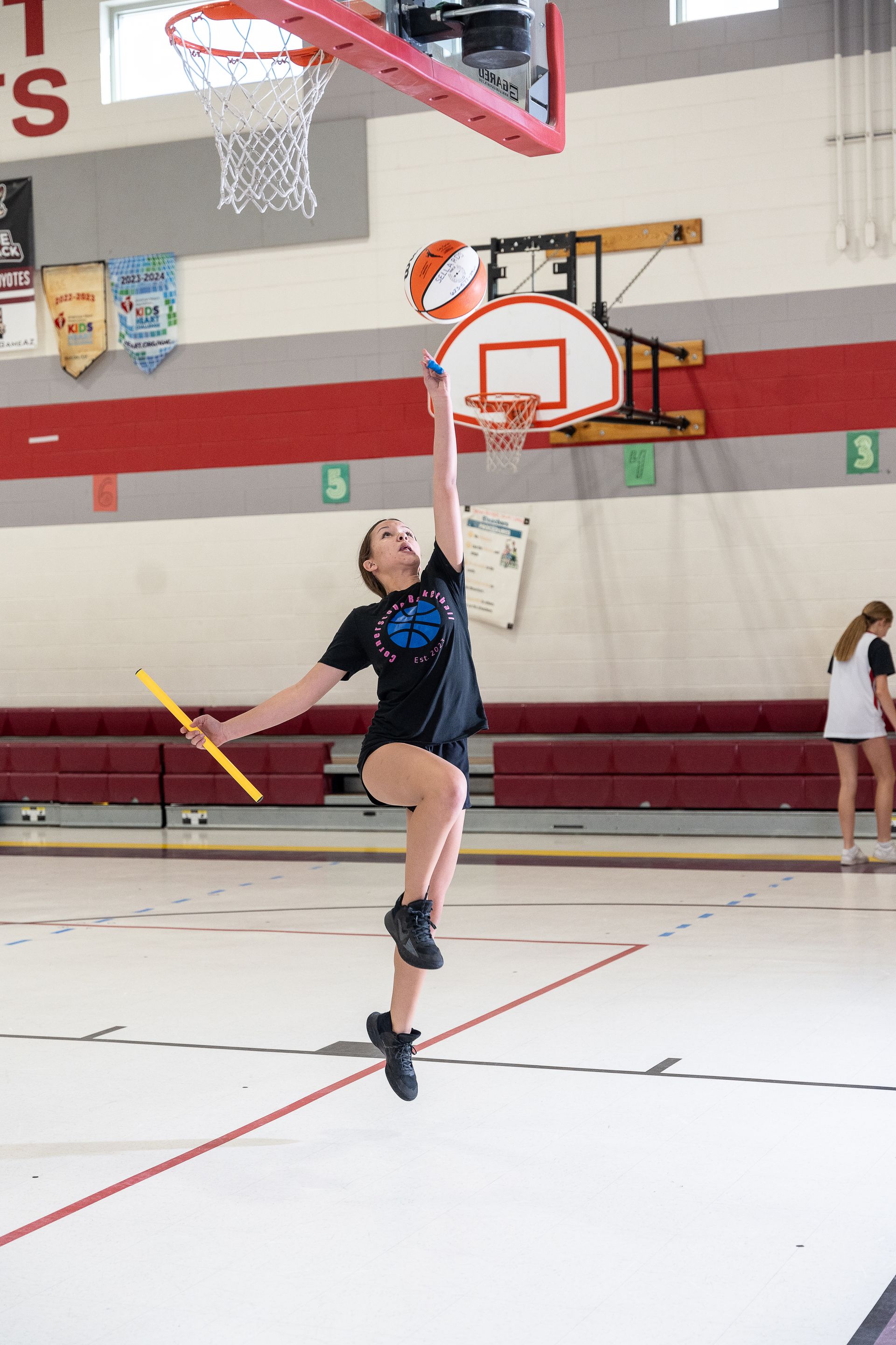 Basketball player leaping for a layup in an indoor gym with a hoop and court lines.