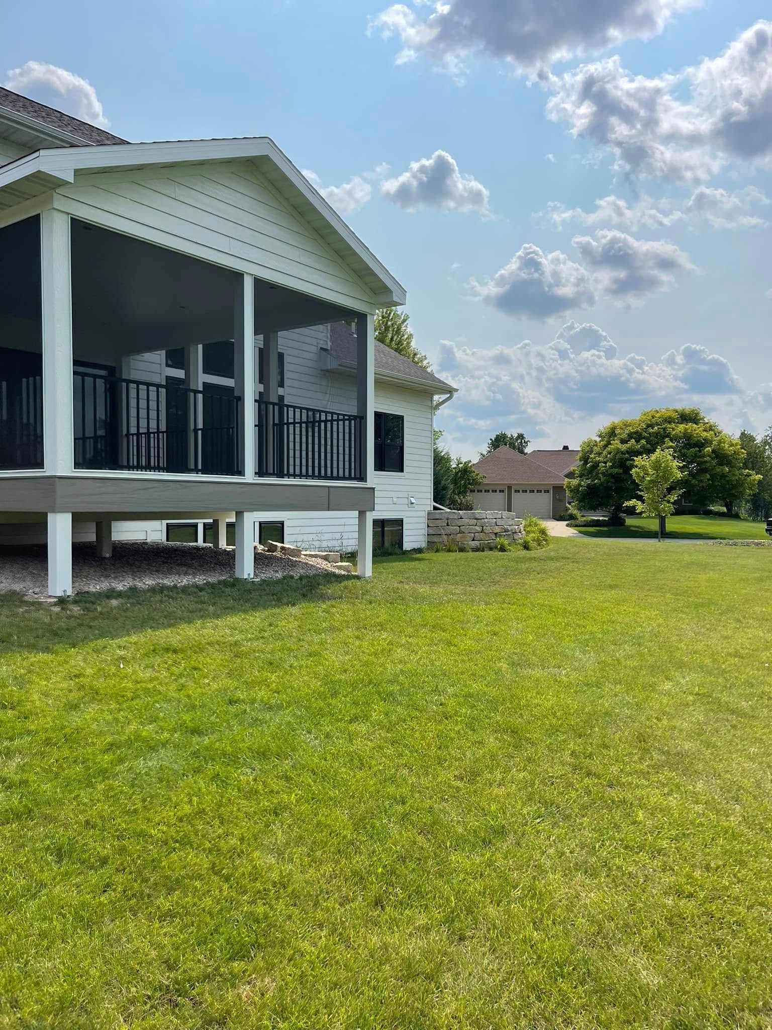 White house with a screened porch and green lawn, sunny day.