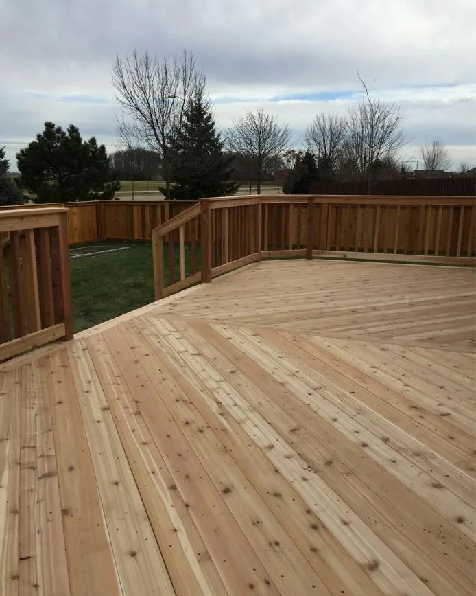 Wooden deck with railings overlooking a yard and trees under a cloudy sky.