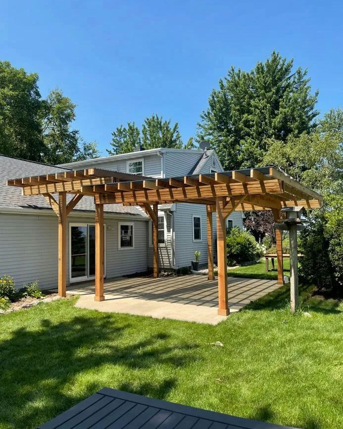 Wooden pergola over a concrete patio next to a house with a green lawn.