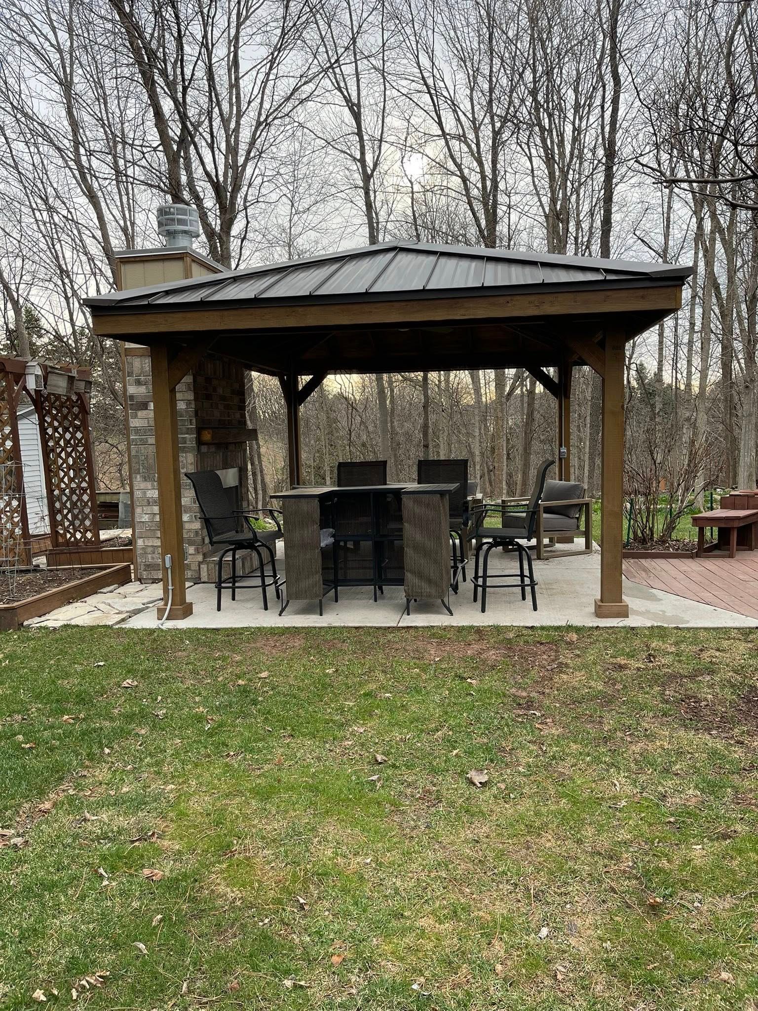 Gazebo with a table and chairs on a concrete patio, with trees in the background.