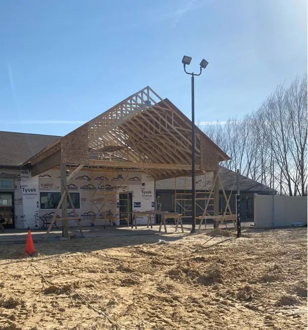 Construction of a wooden awning attached to a building, with exposed rafters and blue sky.