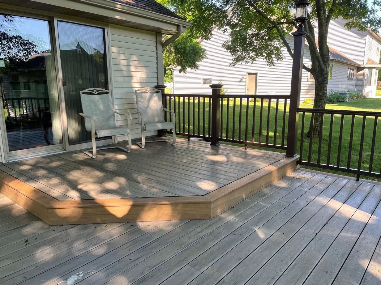 Wooden deck with railing, two chairs, and a sliding glass door.
