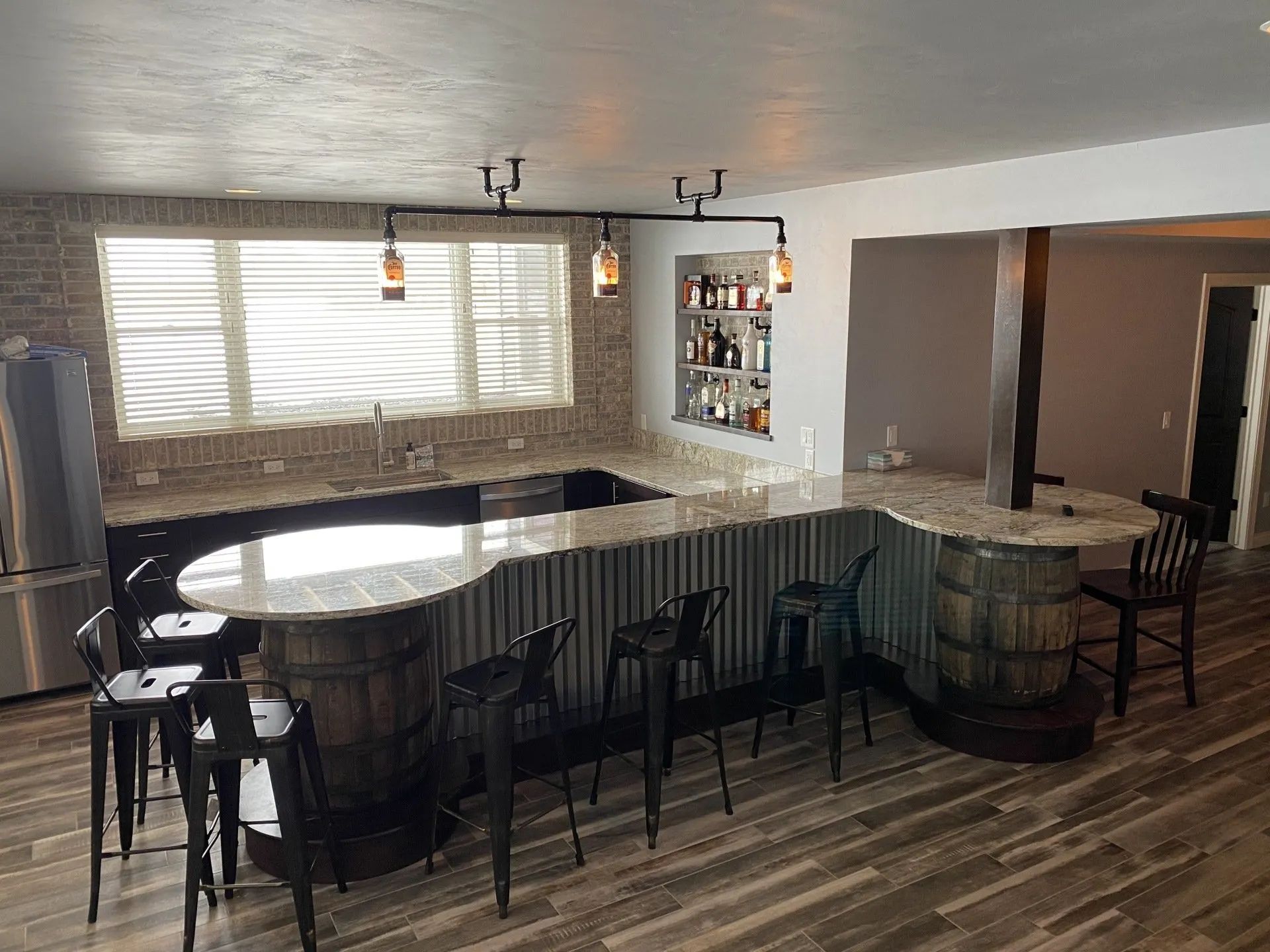 Bar area with corrugated metal siding, barrel-shaped accents, granite countertops, and black bar stools.