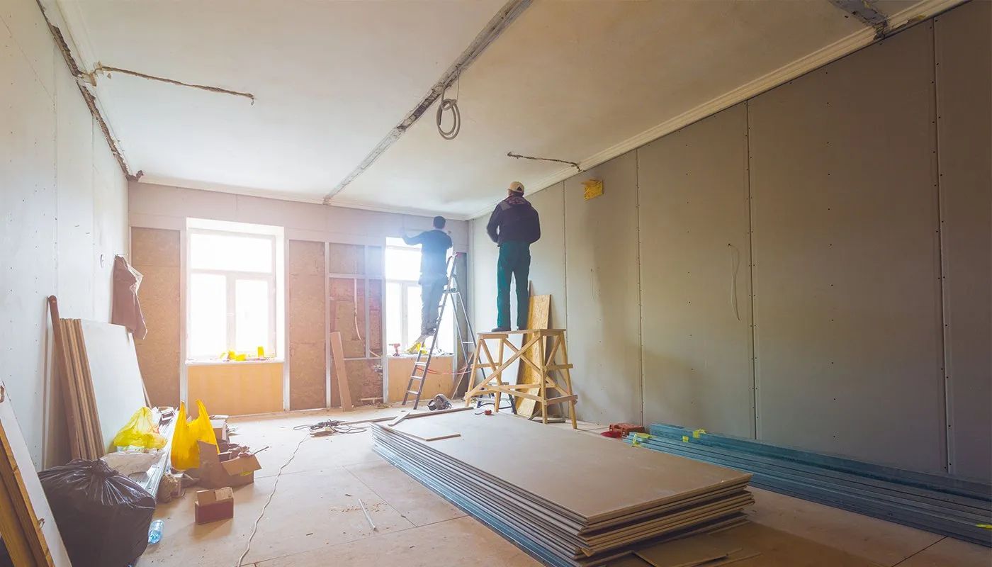 Room under construction with two workers, drywall, and tools.