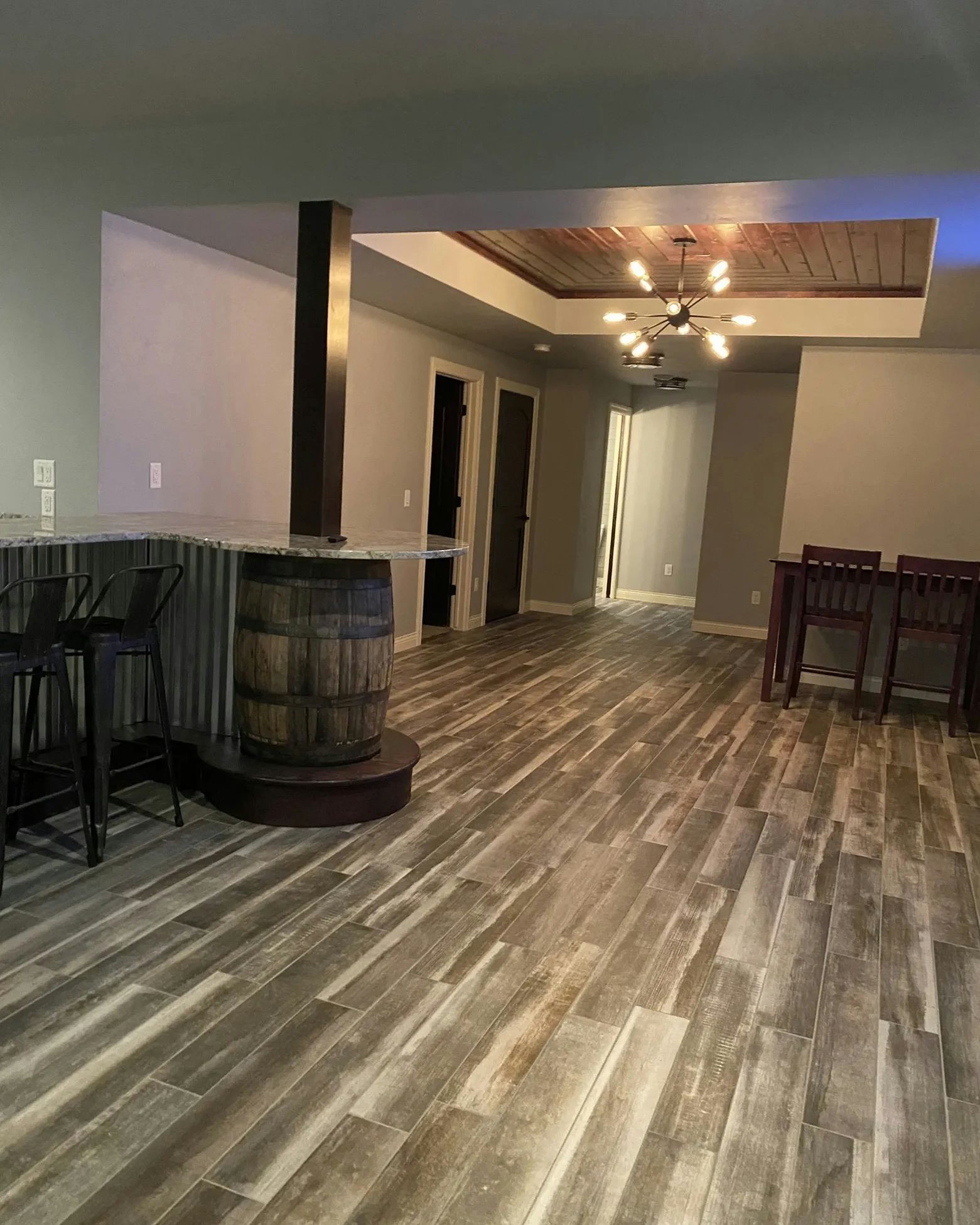 Basement bar area with a wooden barrel bar, gray walls, wood flooring, and a dining table.