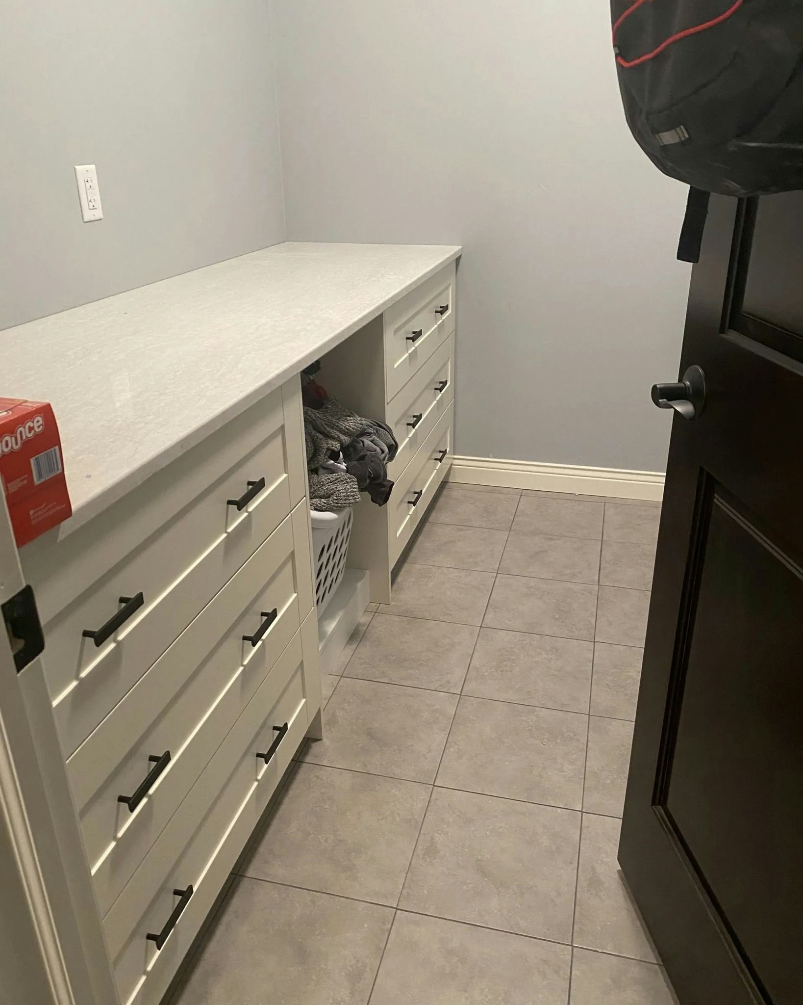 White drawers with black handles, a white countertop, and a gray-tiled floor. Dark door on the right.