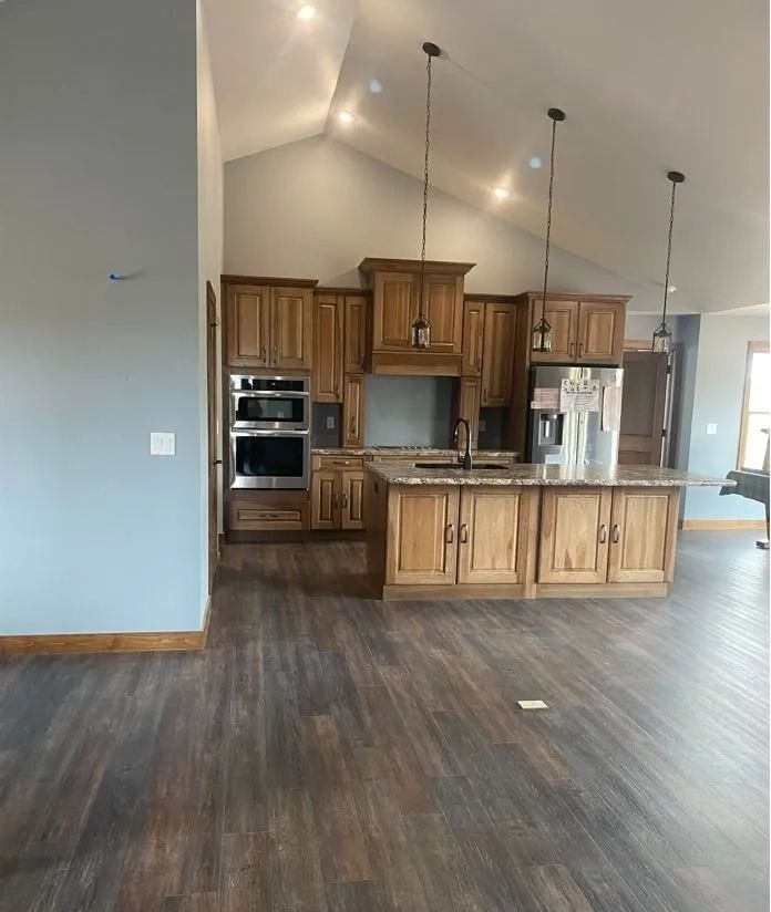 Kitchen with wood cabinets, island, and dark wood flooring. Blue-gray walls, vaulted ceiling.