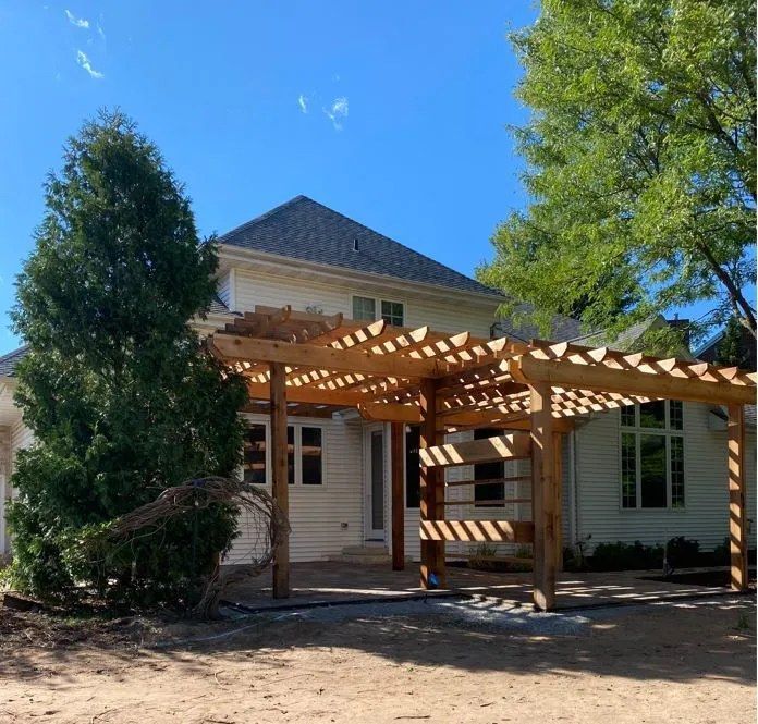 Wooden pergola attached to a white house with a blue sky background.