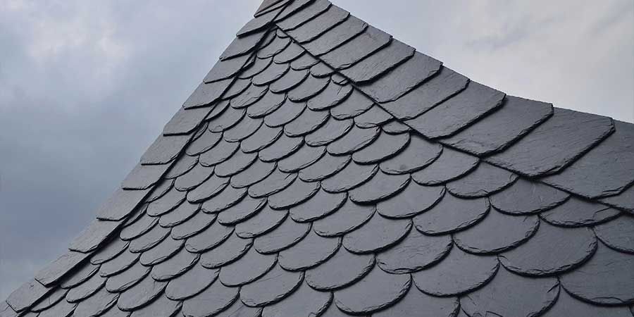 A close up of a roof with slate tiles against a cloudy sky.