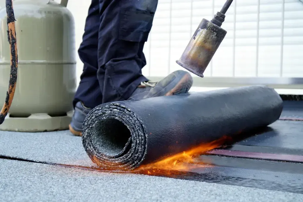 A person is rolling a roll of tpo roofing material on a roof.