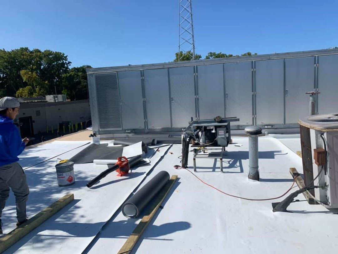 A man is standing on top of a flat roof with tpo roof material.