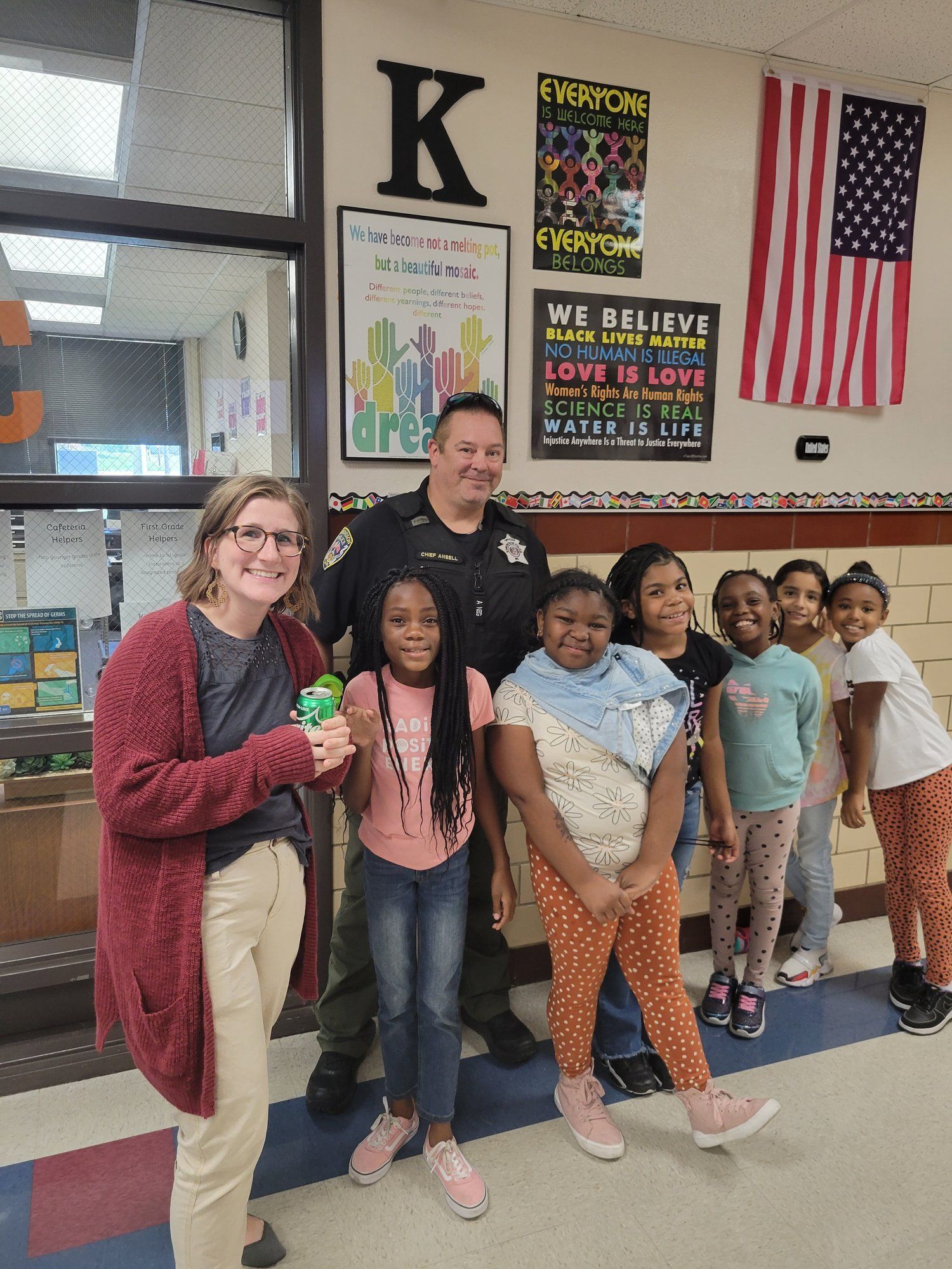 A group of children are posing for a picture with a police officer in a school hallway.