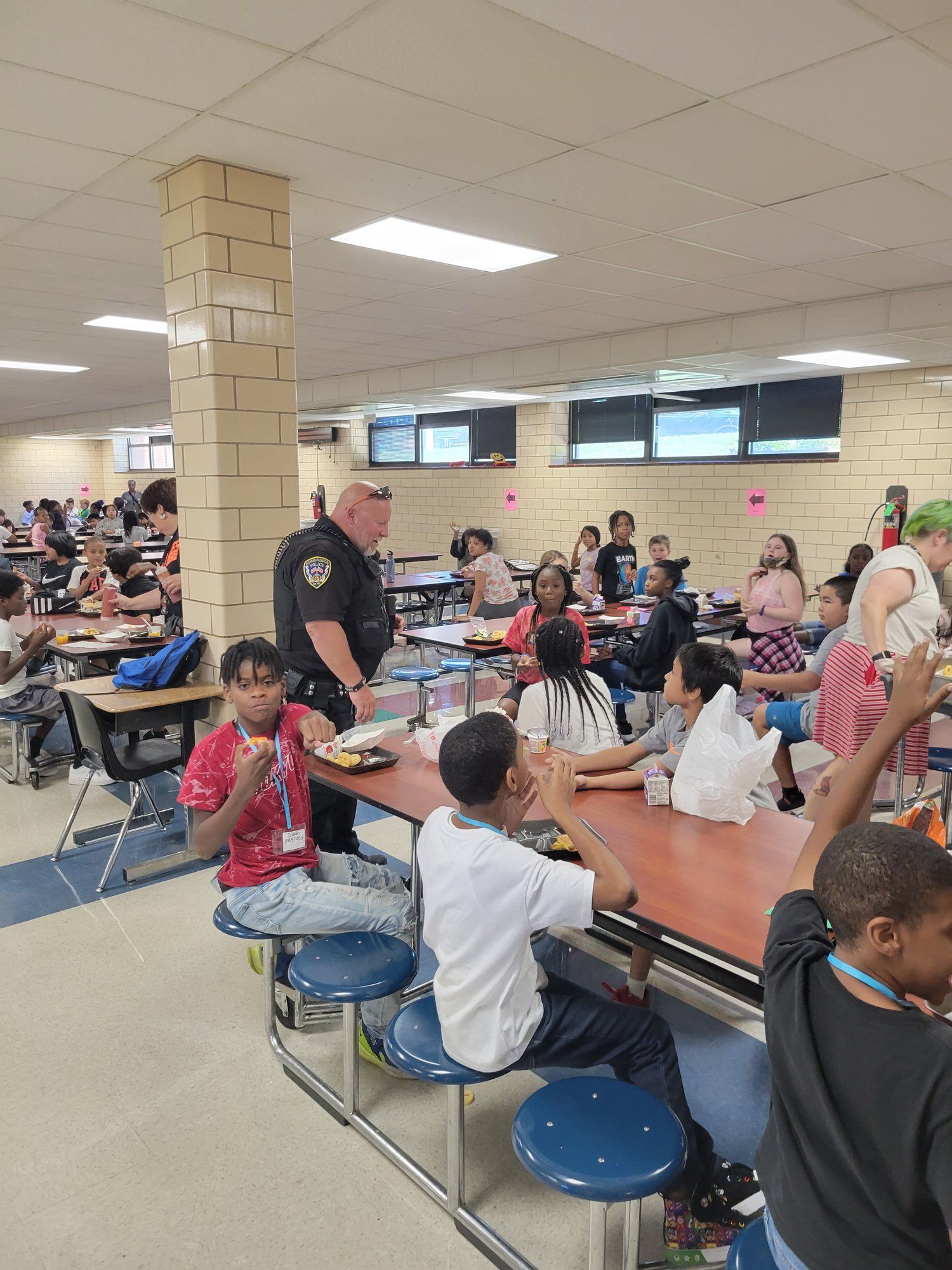 A group of children are sitting at tables in a school cafeteria.