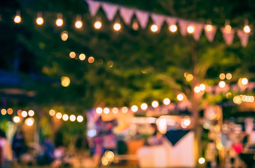 A blurry picture of a festival with lots of lights hanging from the trees.