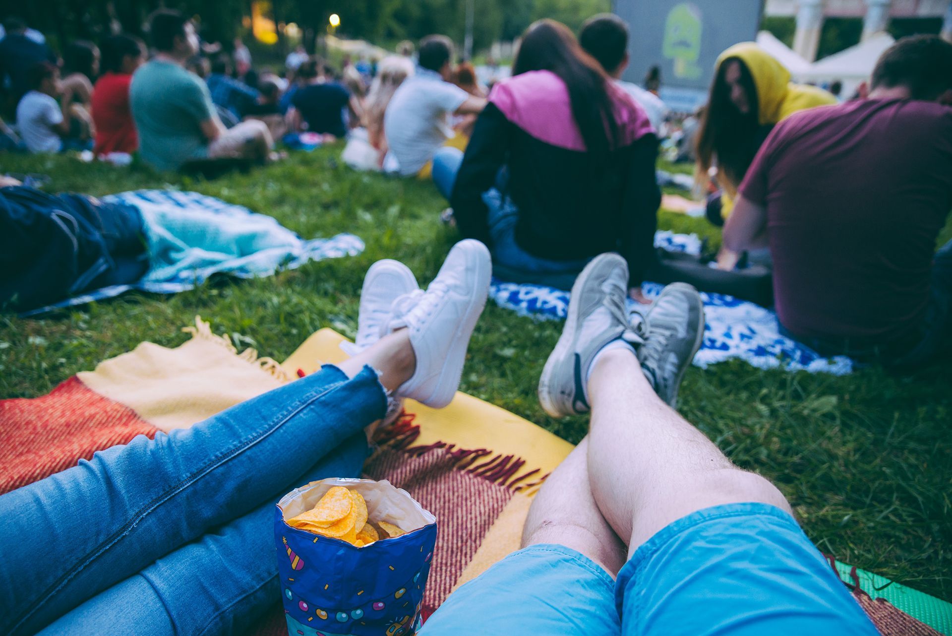 A group of people are sitting on blankets in the grass watching a movie.