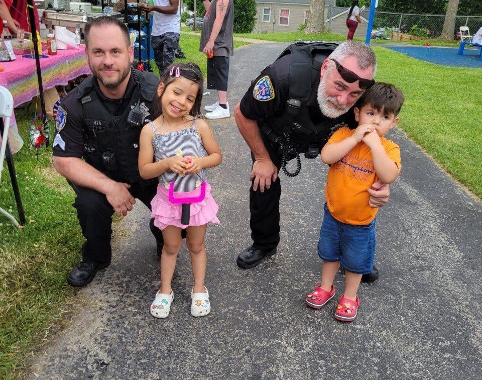 Two police officers are posing for a picture with two children.