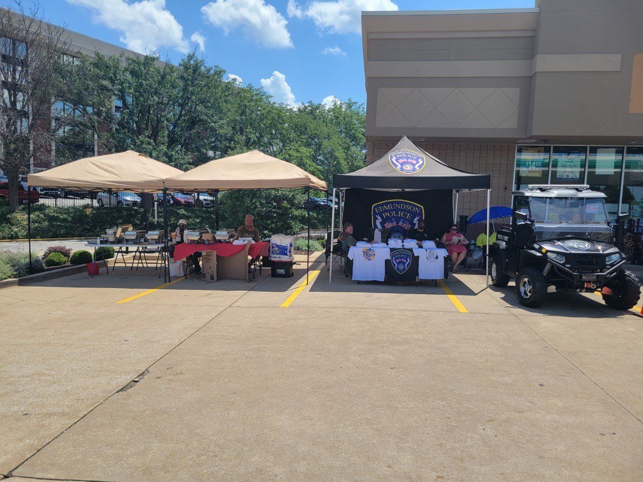 A group of people are sitting under tents in a parking lot.