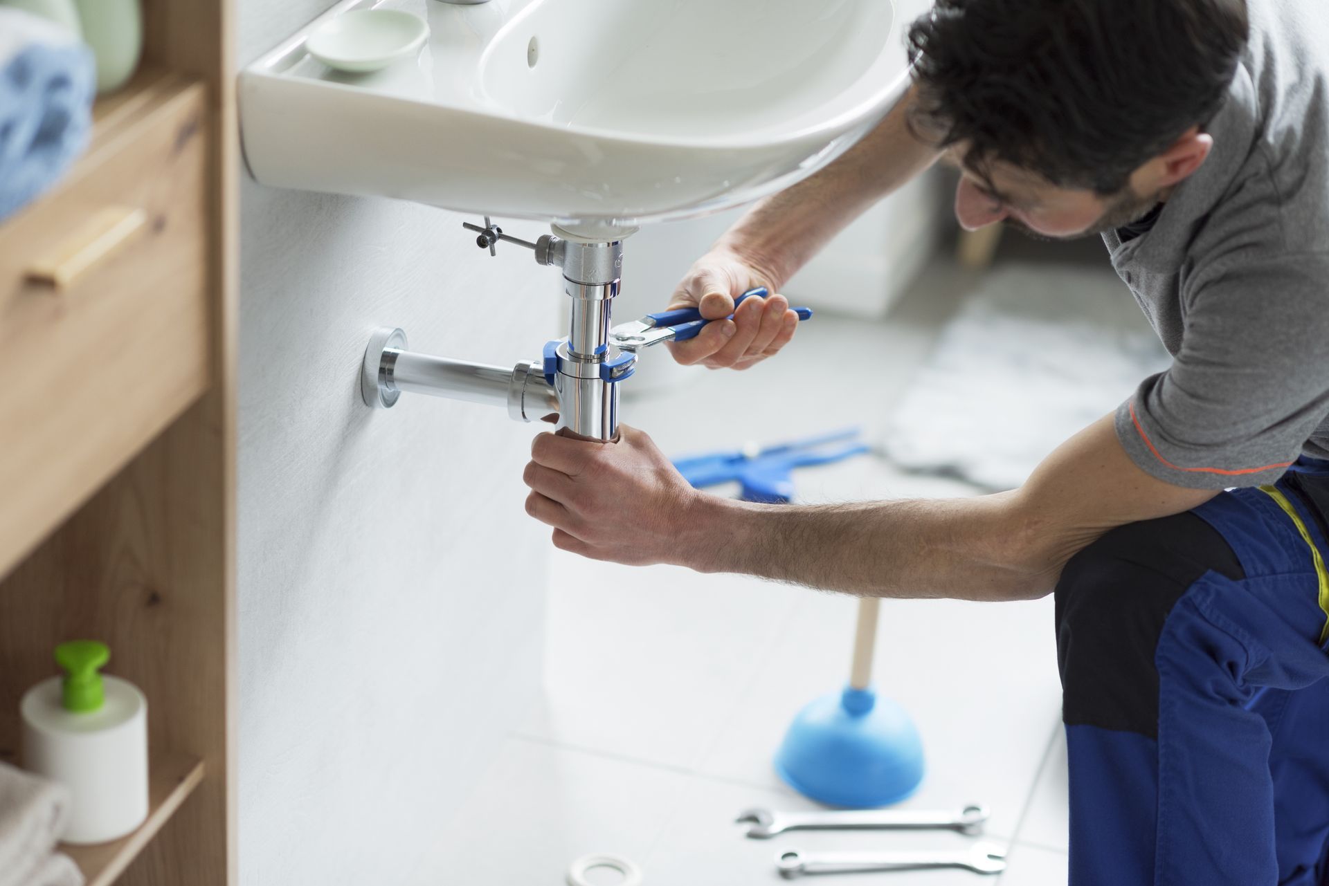 Emergency plumber using a wrench to repair a leaking bathroom sink pipe under the basin. Emergency plumber using a wrench to repair a leaking bathroom sink pipe under the basin.