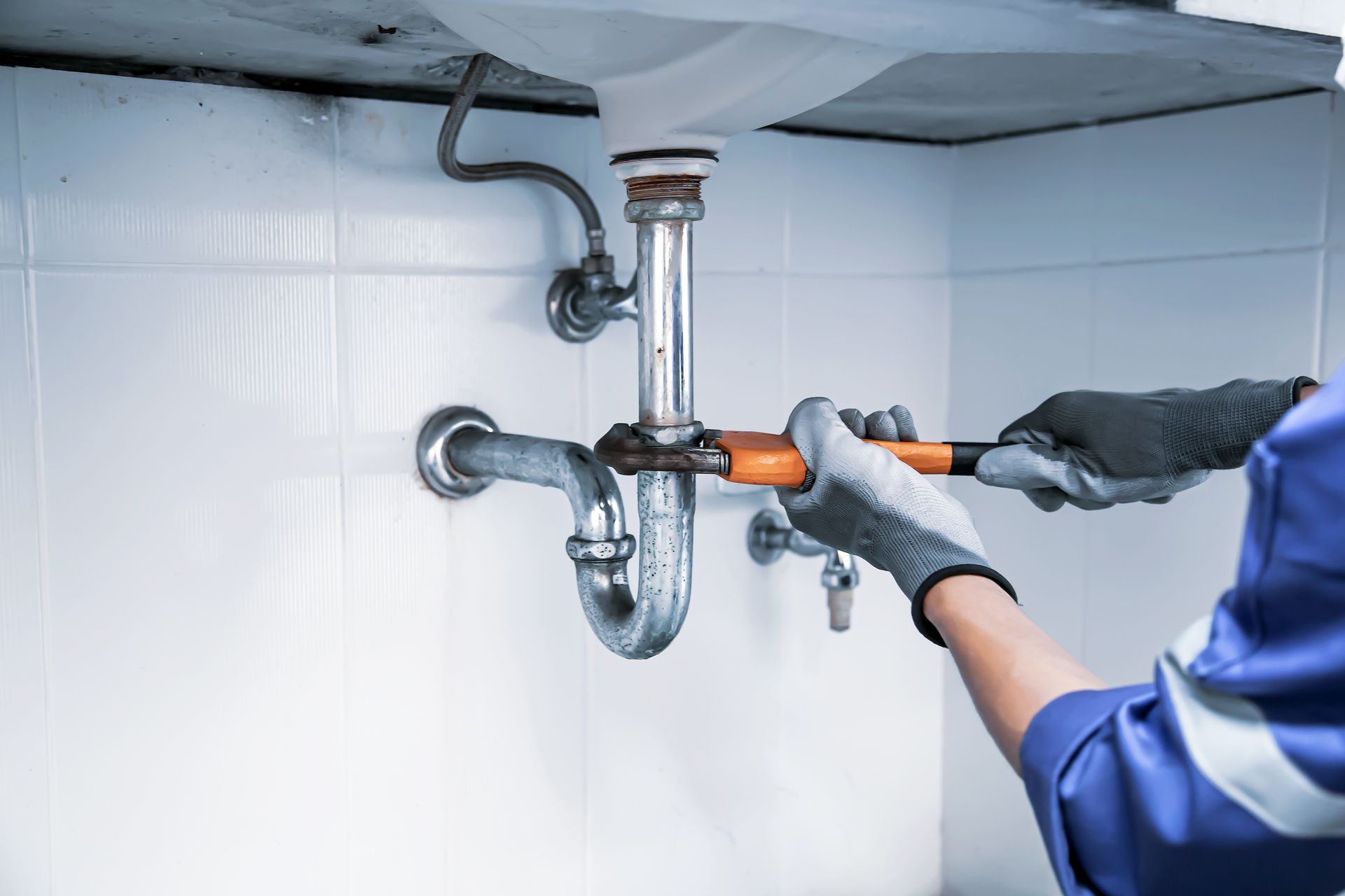 A technician plumber is using a wrench to repair a water pipe under the sink.