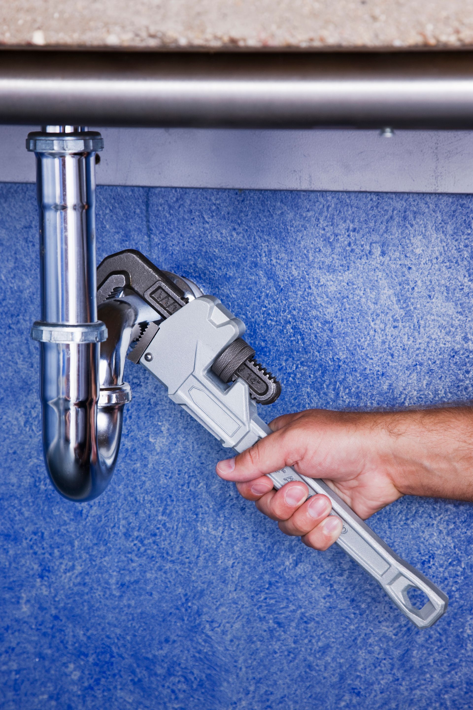 A person holding a wrench under a sink, representing Complete Plumbing's expert plumbing services in