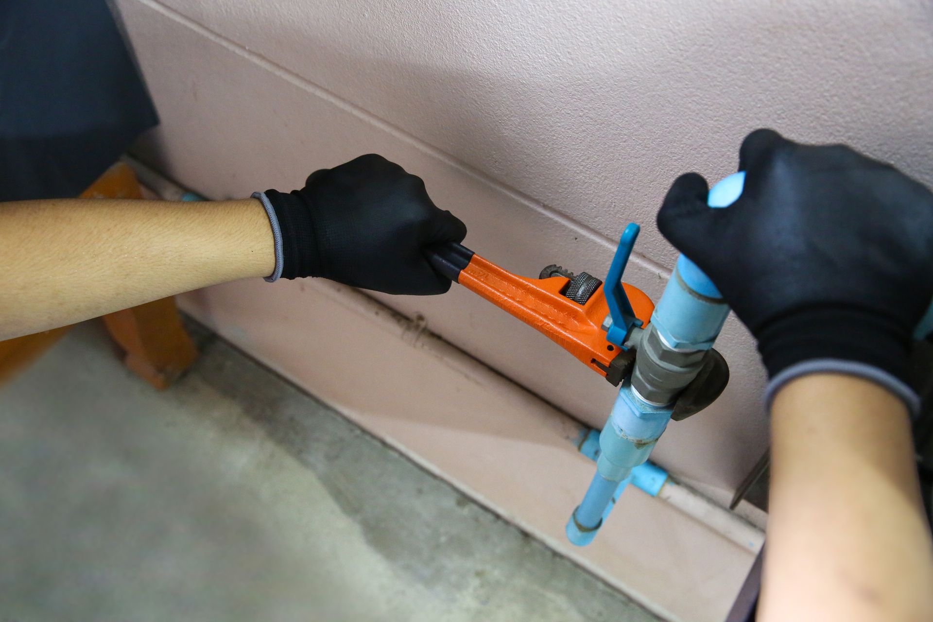 Gloved hands using an orange pipe tool on blue plumbing against a wall with a gray floor Gloved hands using an orange pipe tool on blue plumbing against a wall with a gray floor