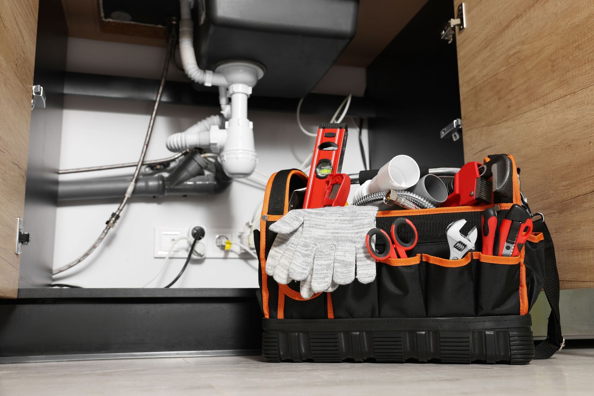 A plumber's black tool bag on the floor under a kitchen sink, used for plumbing services.