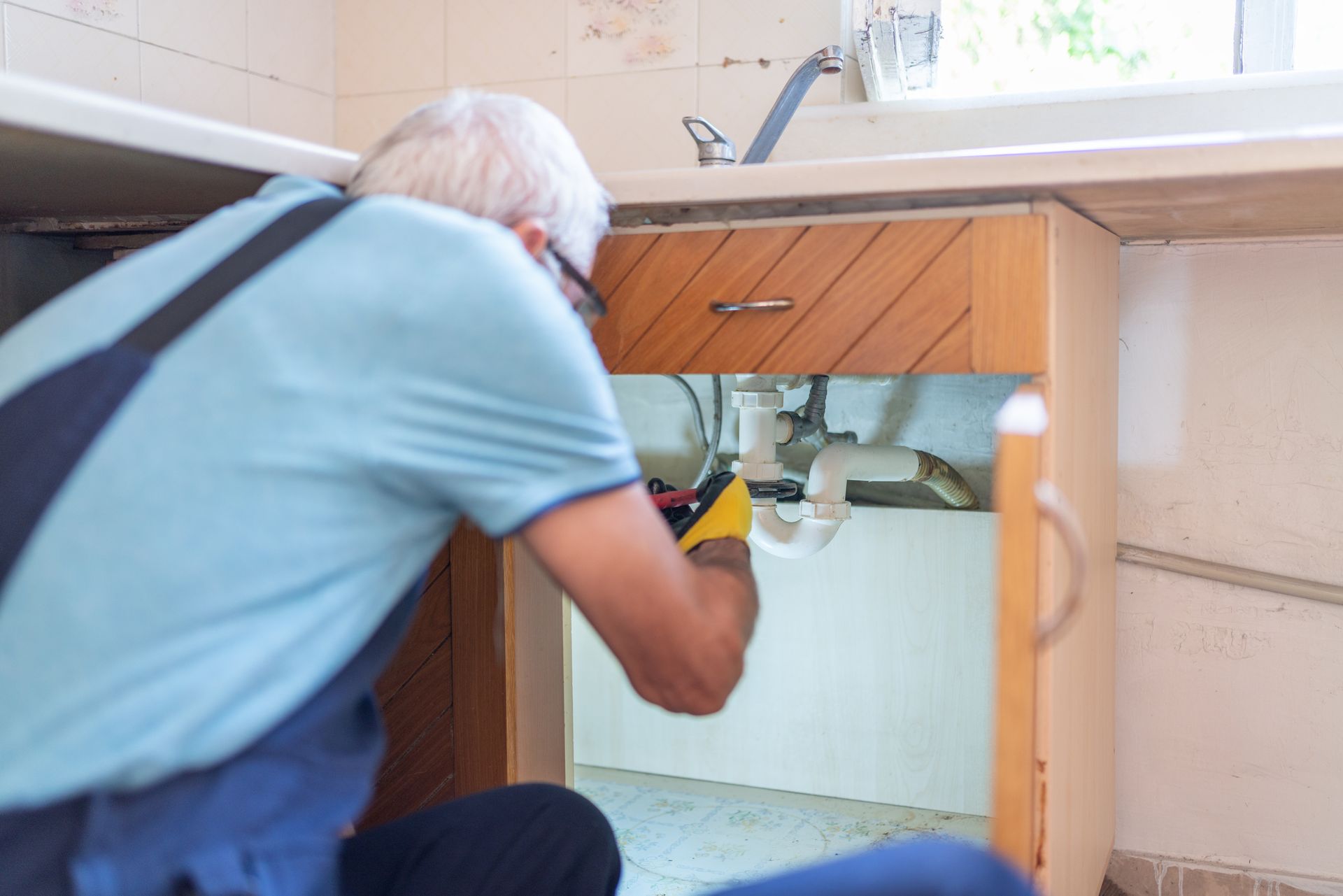 A senior plumber fixing kitchen sink pipes, representing expert plumbing services.