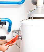 A person is fixing a water heater with a wrench.