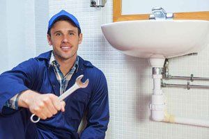 A plumber is sitting in front of a sink holding a wrench.