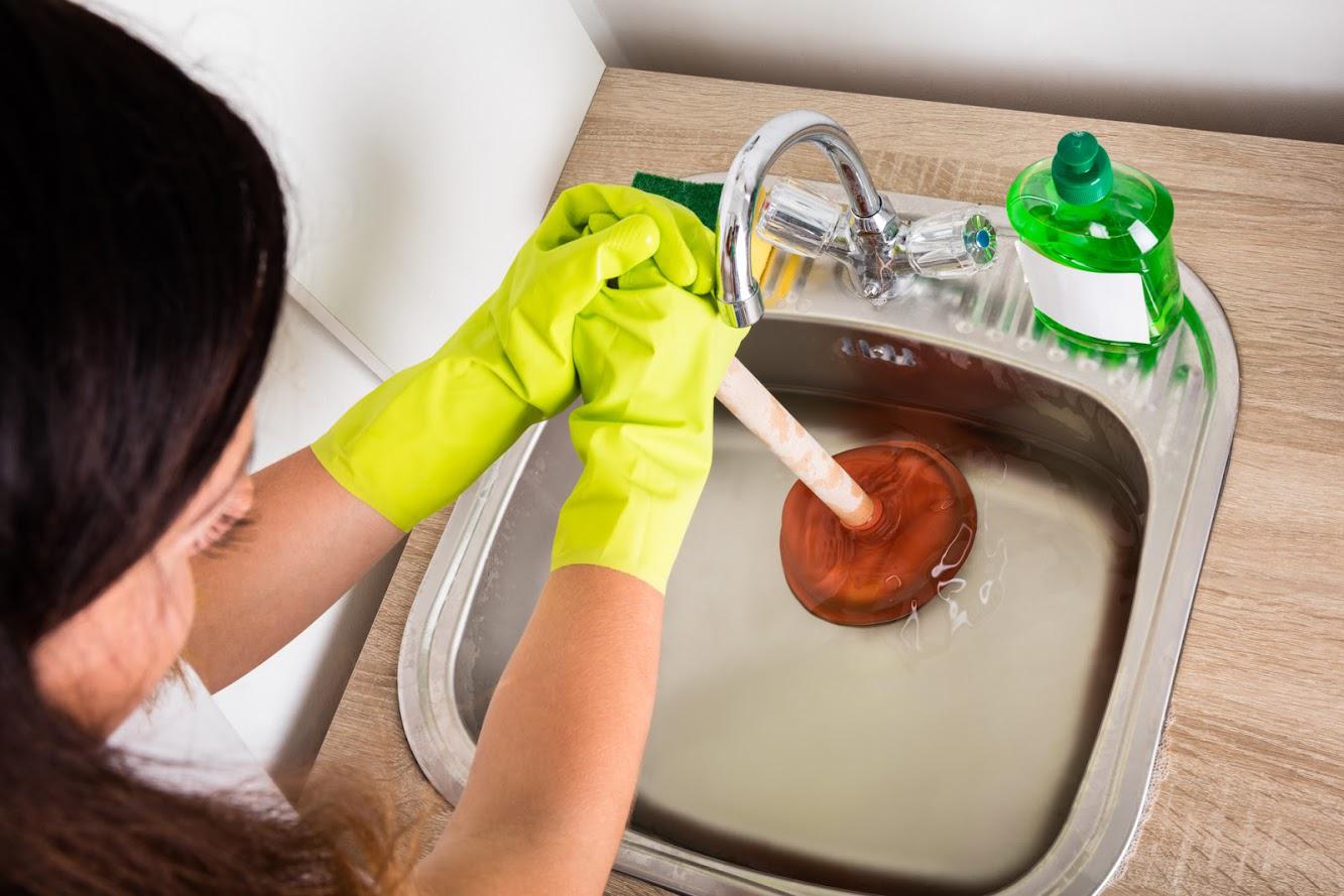 A woman is using a plunger to unblock a sink.