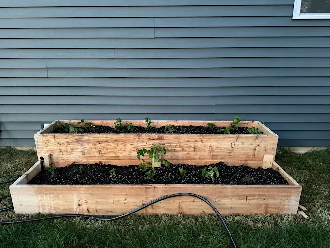 A wooden raised garden bed with a hose attached to it in front of a house.