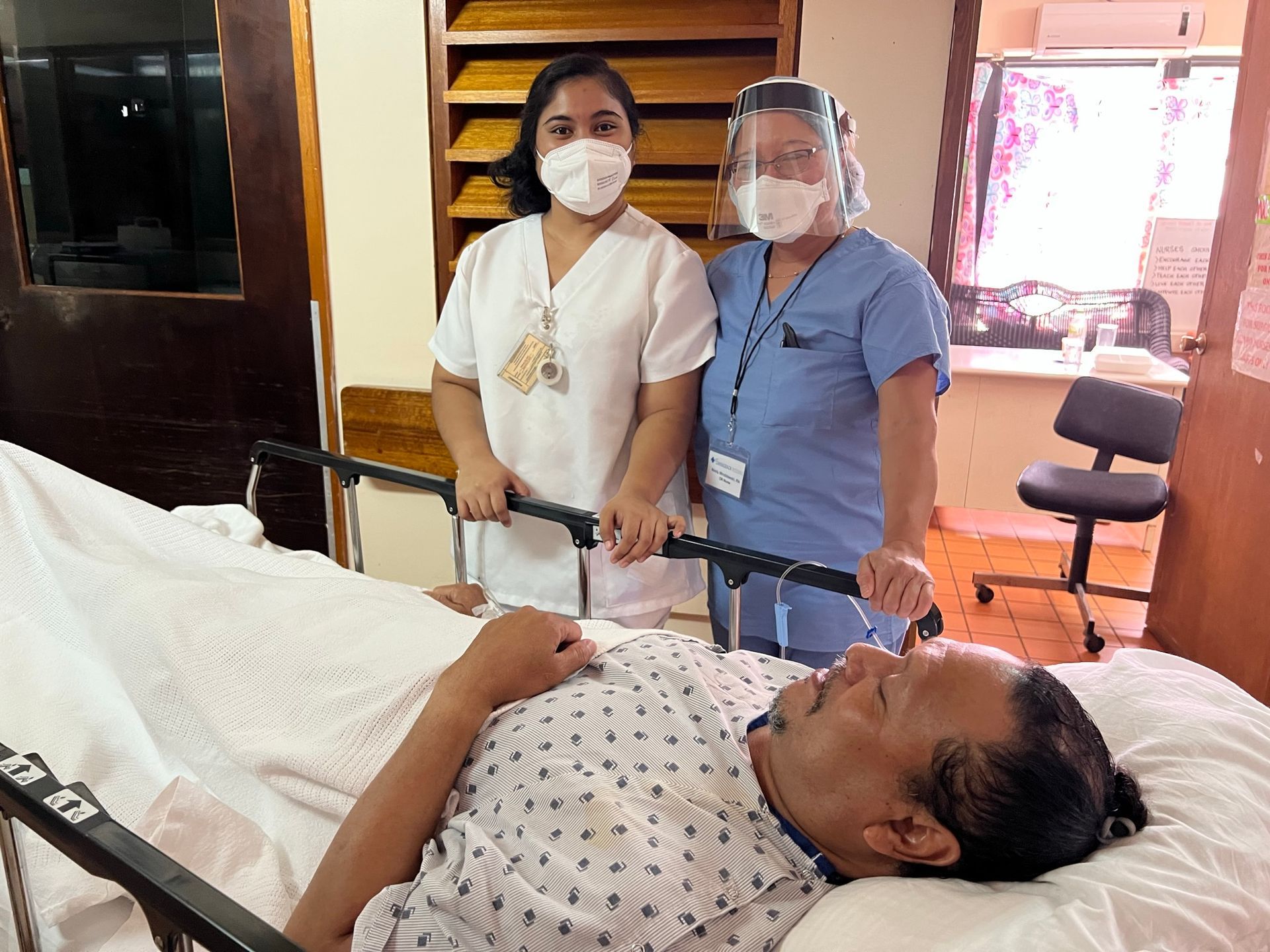 Two nurses are standing next to a patient in a hospital bed.