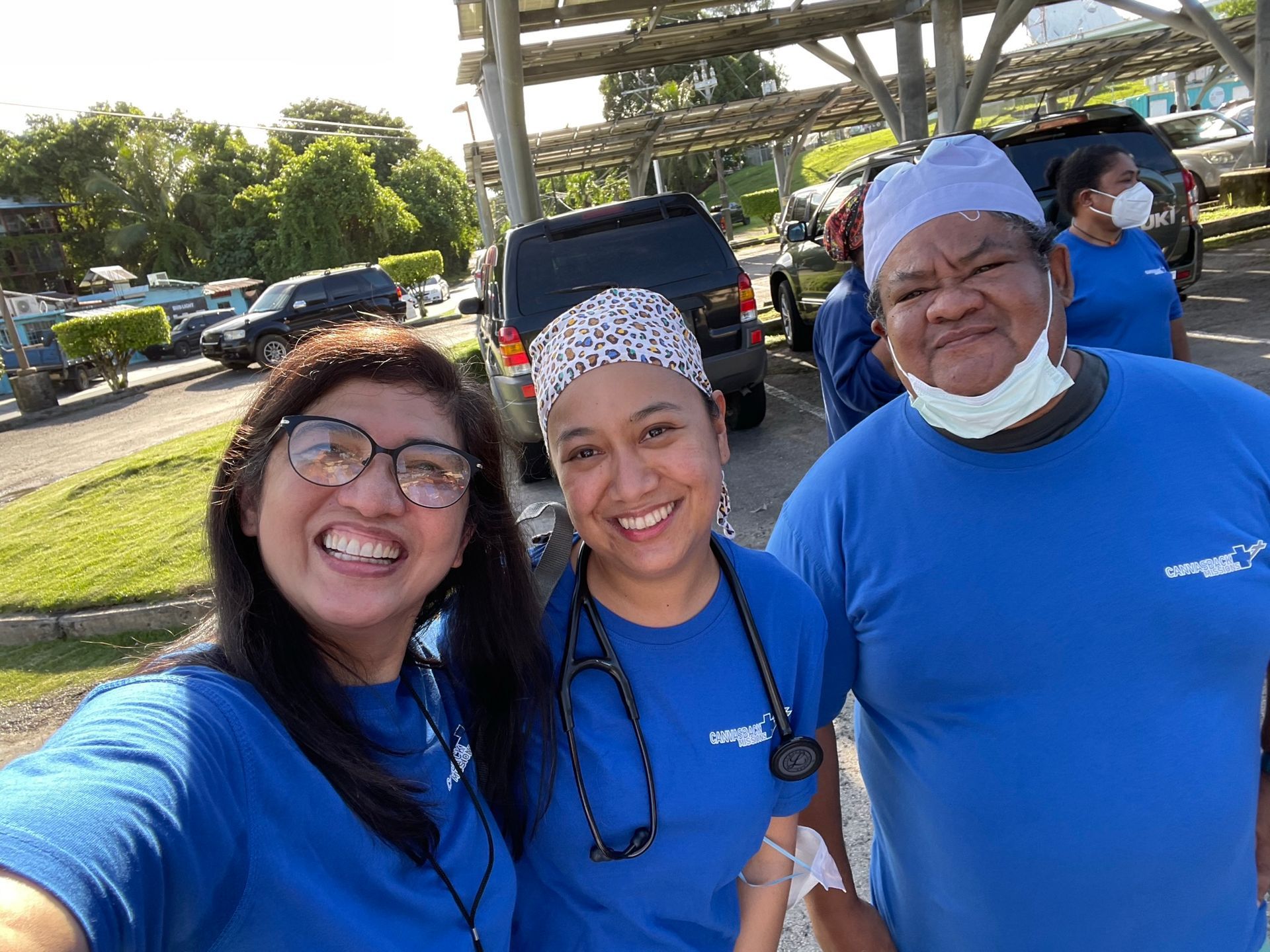Three women wearing blue shirts and masks are posing for a selfie.