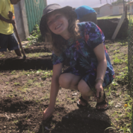 A woman in a hat is squatting down in the dirt.