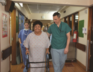 A woman in a hospital gown is walking down a hallway with a walker