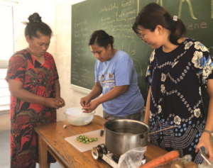 Three women are standing around a table preparing food.