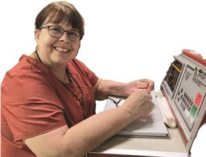 A woman is smiling while sitting at a desk in front of a computer.
