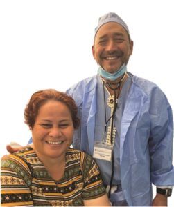 A man in a surgical gown is standing next to a woman in a striped shirt.