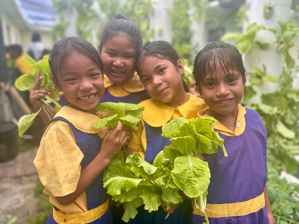 A group of young girls are posing for a picture while holding lettuce.